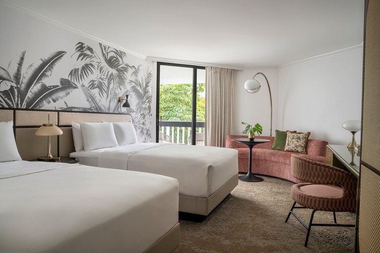 Relaxing two-bed guest room with tropical mural, curved couch and sliding door to balcony at PGA National Resort
