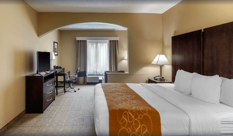 Double bedroom at Comfort Suites The Colony – Plano West with dark wooden furniture, white sheets and orange bed runner