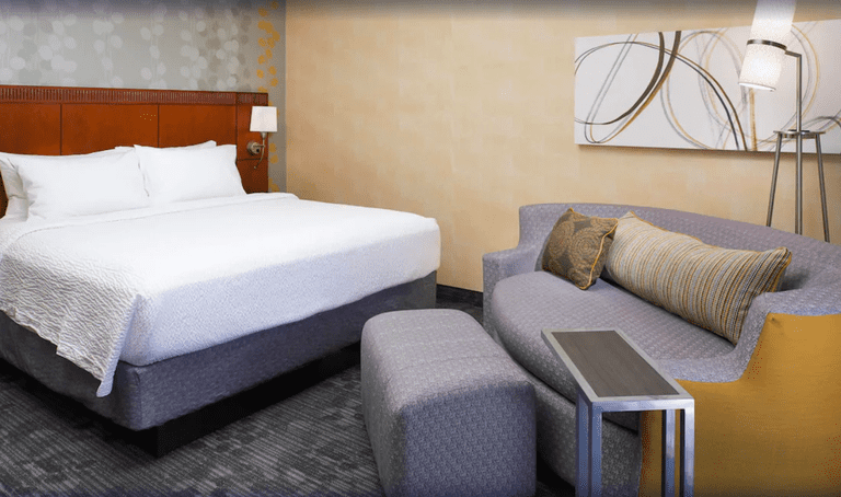 Double bed, sofa and foot stool in a room at Courtyard by Marriott Detroit Dearborn