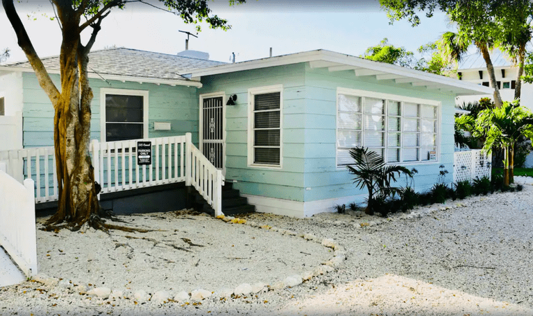 Pale blue cottage fronted by sandy area Rad's Cozy Cottage on Canal in Siesta Key, Florida