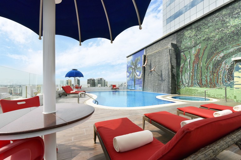 Outdoor swimming pool surrounded by red sun loungers and a mosaic wall at Swiss-Belhotel Seef Bahrain