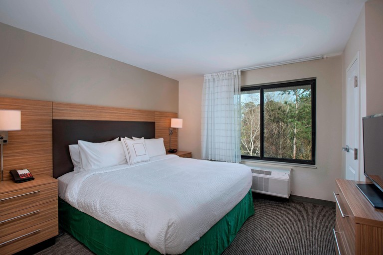 Double bed in a simple room with wooden night stands, a window overlooking trees and a flat screen TV at TownePlace Suites by Marriott Slidell