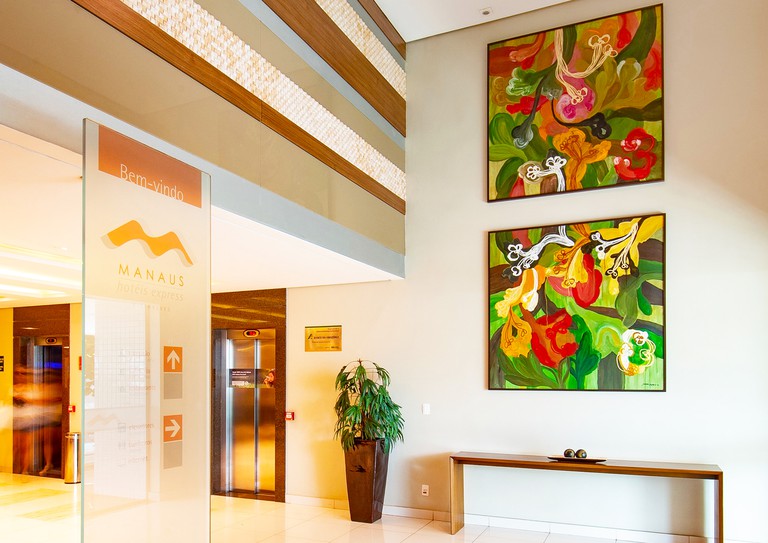 Reception area at Hotel Express Vieiralves featuring large colourful artwork on the walls and an indoor plant