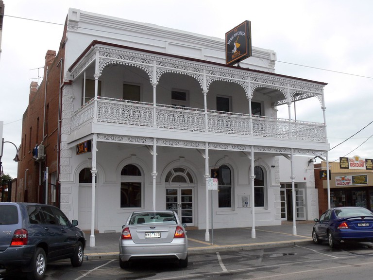 The white Yarrawonga Hotel has two storeys and a pretty, upper balcony with latticed railing, plus car parking in front.