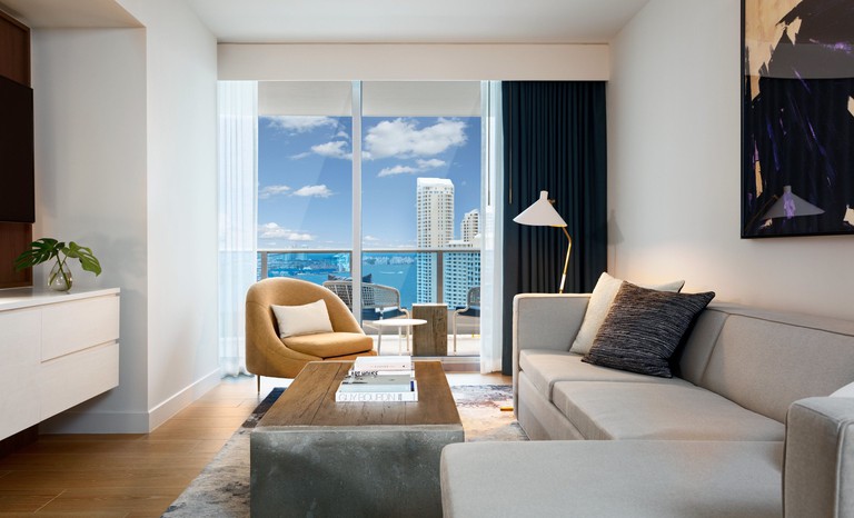 A cozy yet light-filled living room with a sofa, an art piece and a waterfront balcony at the Kimpton EPIC Hotel