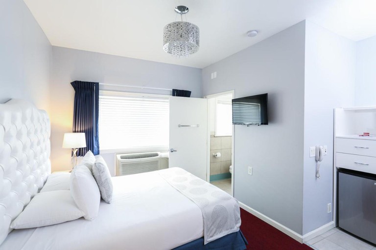 Single bed facing a wall-mounted TV in a white-toned ensuite room at the Hotel Hollywood