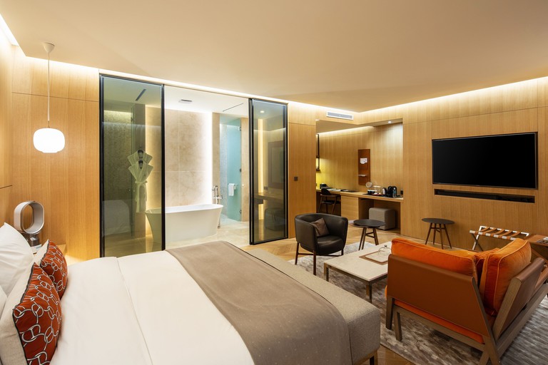 An ensuite bedroom at Hotel 28 Myeongdong with a bed, TV, table, armchairs, modern decor and a bathroom with sliding doors