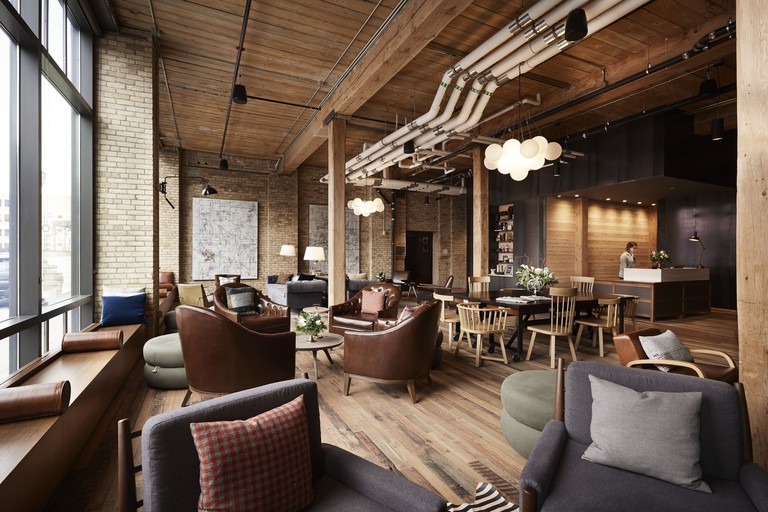 Rustic seating area at Hewing Hotel, with leather and fabric armchairs, wooden floors and ceiling, and exposed-brick walls