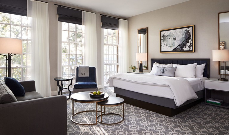 Elegant black and white themed bedroom at The Whitney Hotel with a double bed, sofa, chair, coffee table and floor-to-ceiling windows