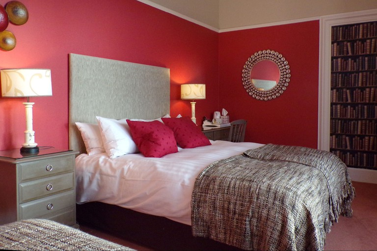 Cosy bedroom with red and light-brown colour scheme, desk and rose-hued carpeting at the Shaftesbury Hotel in Dundee