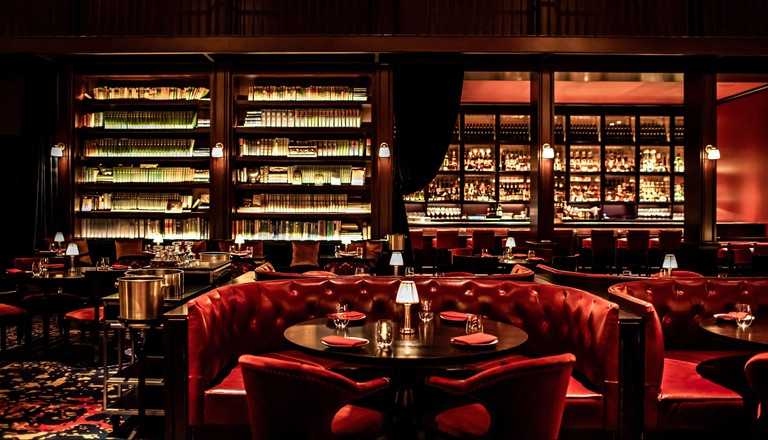 The swanky NoMad Library restaurant with red booths and soaring bookcases at NoMad Las Vegas