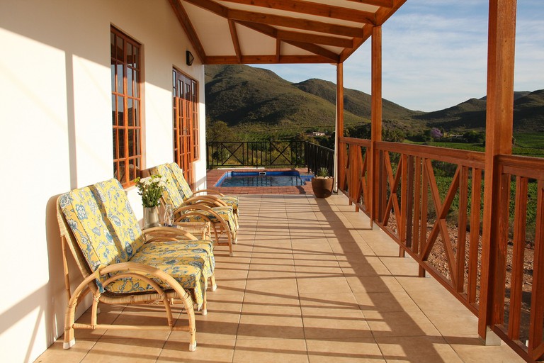 Four cushioned seats on tiled porch with hill views and an outdoor swimming pool at Orange Grove Farm