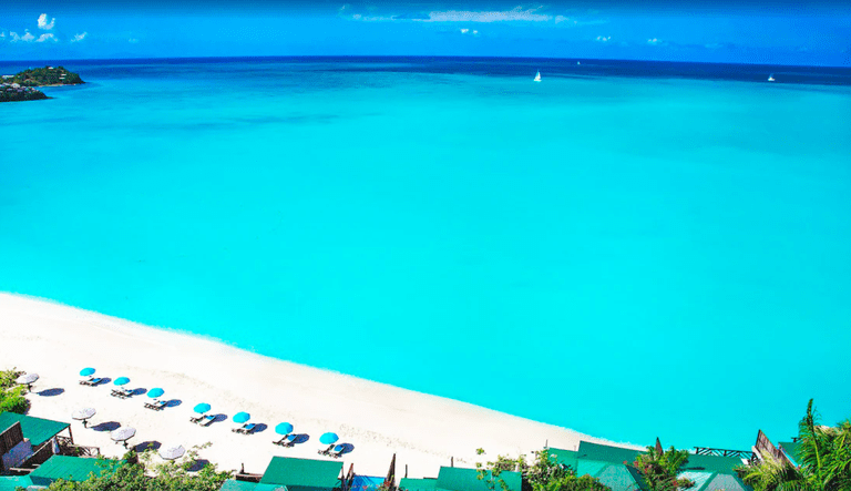 The green rooftops of Cocos Hotel in front of a white-sand beach and stunningly turquoise tranquil seas
