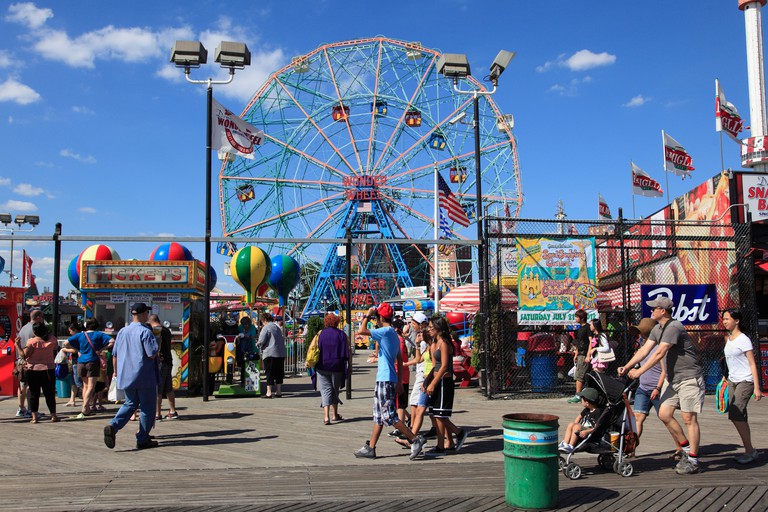 A fun fair with a big colourful wheel, colourful balloons and people walking around at Coney Island, Brooklyn, New York City