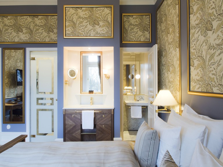 Double bedroom at Grand Hotel with blue walls and frames filled with floral wallpaper and a marble bathroom