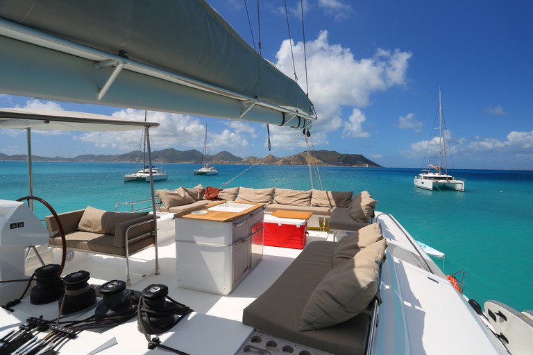 Cushioned seating on the desk of a catamaran sailing in bright blue waters, with other boats nearby