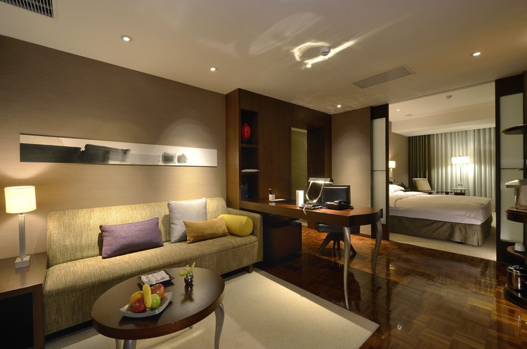 Stylish double bedroom in suite at Les Suites Taipei with muted colour palette, light green sofa and dark wooden floor