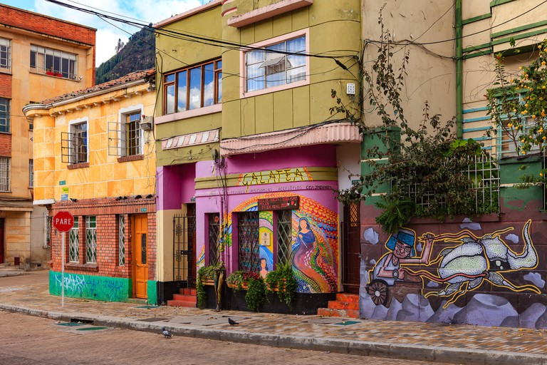 Colorful building facades in La Candelaria adorned with vibrant murals, with brick-lined sidewalks and roads in front