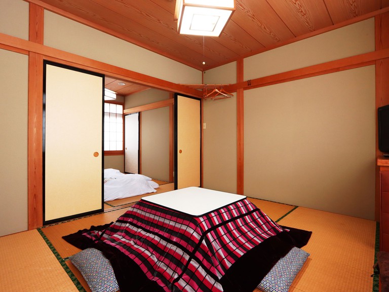 A traditional dining space with pillows around a table, tatami mats and sliding doors to bedroom at Minshuku Kojima