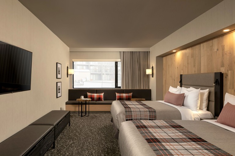 Cozy yet modern guest room with two beds, wood accent wall, plaid accents and dark brown seating at Peaks Hotel and Suites