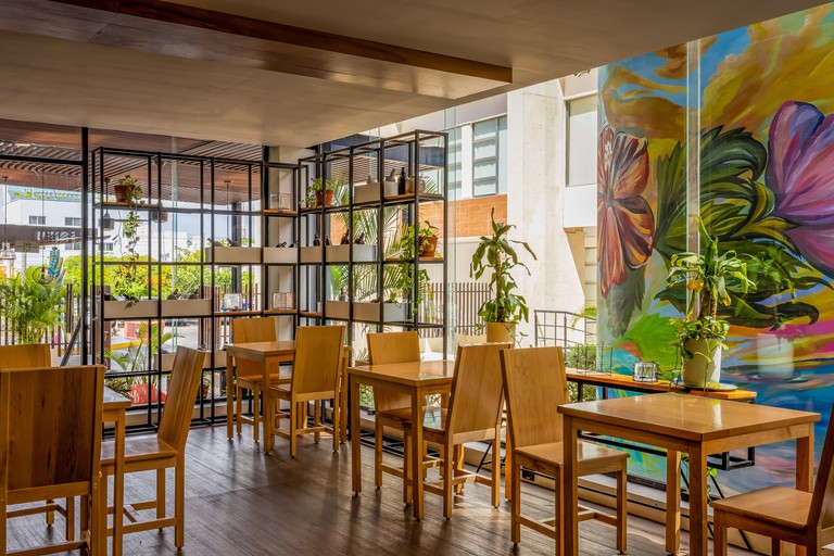 Pleasant dining space with natural wood tables and chairs, plants and floor-to-ceiling windows at Wyndham Garden Cancun Downtown