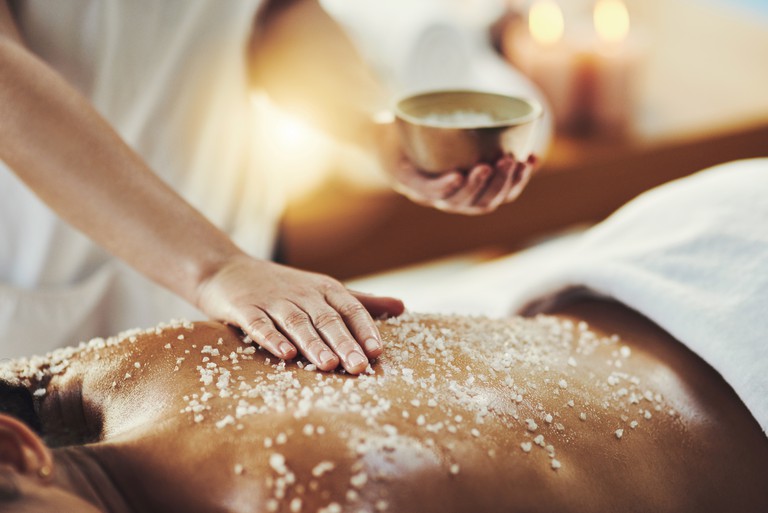 A woman lying on her stomach gets a body scrub by a masseuse