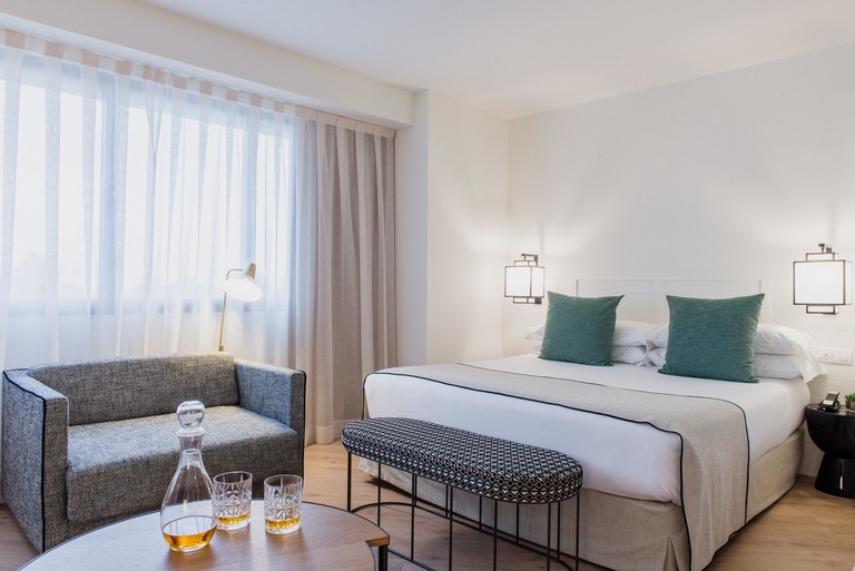 Double bedroom with white linen, a smart grey sofa and two glasses of whisky at Hotel Molina Lario