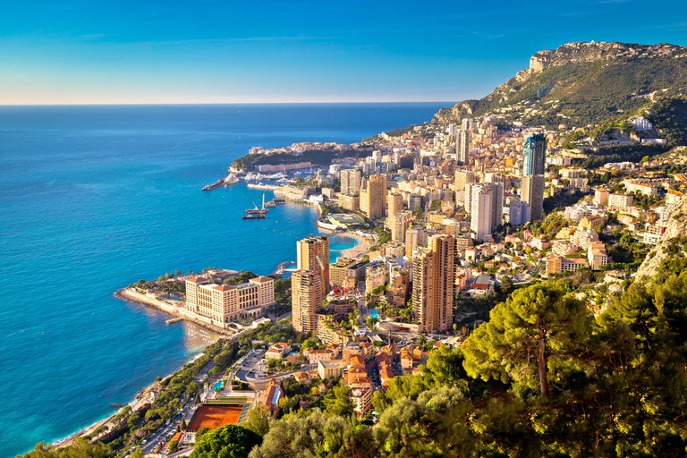 View from above of Monte Carlo cityscape built into the mountainside with skyscrapers and a large harbour